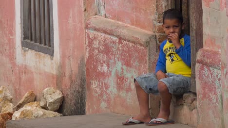 Un-Niño-Se-Sienta-En-La-Calle-Mirando-A-Los-Transeúntes-En-Trinidad,-Cuba