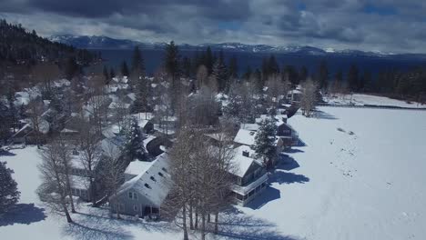 Una-Antena-Sobre-Un-Pueblo-Cubierto-De-Nieve-En-Las-Montañas-De-Sierra-Nevada-Con-El-Lago-Tahoe-Ion-Al-Fondo