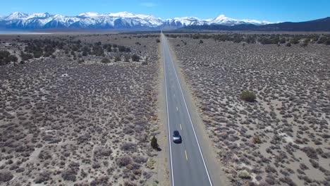 Aerial-above-a-4WD-traveling-on-a-paved-road-in-the-Mojave-Desert-with-the-Sierra-Nevada-mountains-distant