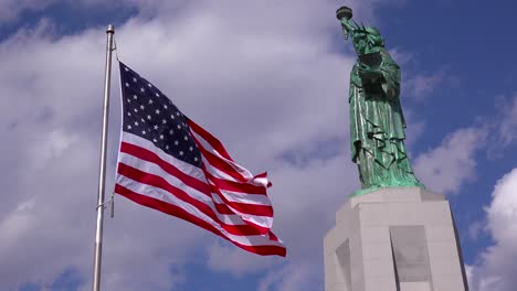 Eine-Patriotische-Aufnahme-Der-Freiheitsstatue-Vor-Einem-Bewölkten-Himmel-Mit-Der-Amerikanischen-Flagge-Im-Vordergrund