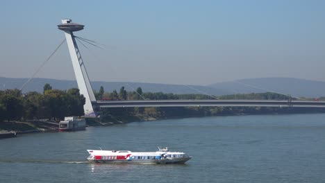 Eine-Fähre-Manövriert-Auf-Der-Donau-Mit-Der-Modernen-Brücke-In-Bratislava-Slowakei-Hintergrund