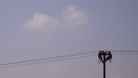 Two-men-in-silhouette-work-on-an-electrical-cable-atop-a-telephone-pole-1