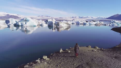 Antenne-Einer-Frau,-Die-Entlang-Des-Ufers-Einer-Gletscherlagune-In-Der-Arktis-An-Der-Jökulsarlon-Gletscherlagune-Island-Steht-4