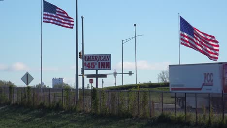 Un-Camionero-De-Larga-Distancia-Pasa-Por-Un-Hotel-Económico-Y-Banderas-Estadounidenses-A-Lo-Largo-De-Una-Autopista-Interestatal-De-Estados-Unidos-En-América