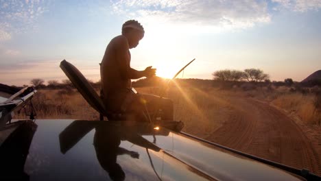 Un-Guía-Nativo-De-Observación-Se-Sienta-En-La-Parte-Delantera-De-Un-Vehículo-Jeep-Safari-Para-Observar-La-Vida-Silvestre-En-Las-Llanuras-De-África-Al-Atardecer