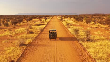 Antenne-Eines-Safari-Jeeps,-Der-Auf-Den-Ebenen-Afrikas-Im-Erindi-Wildreservat-In-Namibia-Reist,-Mit-Einem-Einheimischen-San-Tribal-Spotter-Führer,-Der-Auf-Der-Vorderseite-Sitzt-und-Wildtiere-Beobachtet