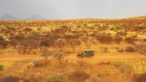 Antenne-Eines-Safari-Jeeps,-Der-Auf-Den-Ebenen-Afrikas-Im-Erindi-Wildreservat-In-Namibia-Reist,-Mit-Einheimischem-San-Tribal-Spotter-Führer,-Der-Auf-Der-Vorderseite-Sitzt-Und-Wildtiere-Beobachtet-1