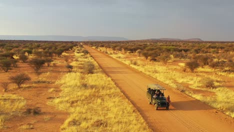 Antenne-Eines-Safari-Jeeps,-Der-Auf-Den-Ebenen-Afrikas-Im-Erindi-Wildreservat-In-Namibia-Reist,-Mit-Einheimischem-San-Tribal-Spotter-Führer,-Der-Auf-Der-Vorderseite-Sitzt-Und-Wildtiere-Beobachtet-3