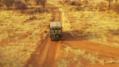 Antenne-Eines-Safari-Jeeps,-Der-Auf-Den-Ebenen-Afrikas-Im-Erindi-Wildreservat-In-Namibia-Reist,-Mit-Einheimischem-San-Tribal-Spotter-Führer,-Der-Auf-Der-Vorderseite-Sitzt-Und-Wildtiere-Beobachtet-5