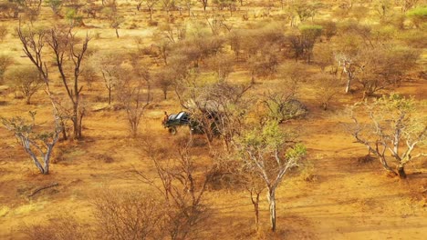 Excelente-Antena-De-Un-Jeep-Safari-Que-Viaja-Por-Las-Llanuras-De-áfrica-En-Erindi-Game-Reserve-Namibia-Con-Un-Guía-Nativo-De-San-Tribales-Sentado-En-El-Frente-Observando-La-Vida-Silvestre