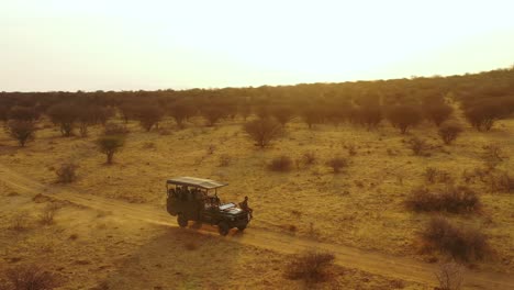 Antenne-Eines-Safari-Jeeps,-Der-Auf-Den-Ebenen-Afrikas-Im-Erindi-Wildreservat-In-Namibia-Reist,-Mit-Einheimischem-San-Tribal-Spotter-Führer,-Der-Auf-Der-Vorderseite-Sitzt-Und-Wildtiere-Beobachtet-8