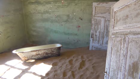 Sand-and-a-bath-tub-fills-an-abandoned-building-in-the-gem-mining-ghost-town-of-Kolmanskop-Namibia