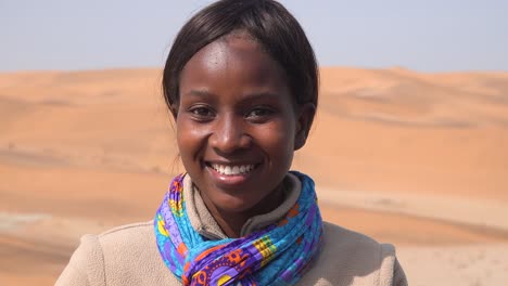 Nahaufnahme-Eines-Schönen-Jungen-Frauenmodells-Aus-Namibia,-Das-Mit-Sanddünen-Im-Hintergrund-Lächelt