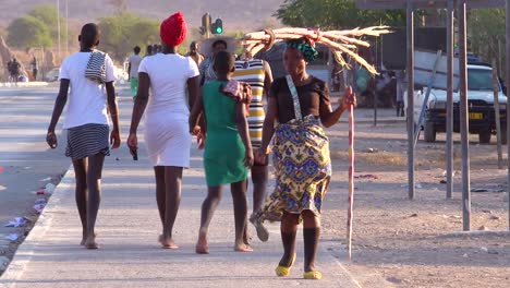 Eine-Stammesfrau-Geht-Durch-Die-Straßen-Einer-Marktstadt-In-Afrika-Opuwo-Namibia-Mit-Brennholz-Auf-Dem-Kopf