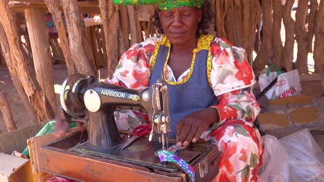 Eine-Afrikanische-Herero-Stammesfrau-In-Hellen-Modekostümen-Betreibt-Eine-Antike-Nähmaschine-Auf-Einem-Marktplatz-In-Namibia-Afrika-1