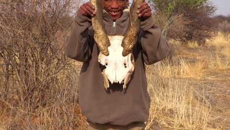 Un-Cazador-De-Bosquimanos-De-San-Recoge-Y-Muestra-El-Cráneo-De-Un-Animal-En-Las-Llanuras-De-África