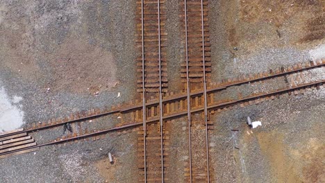 Vista-Aérea-looking-straight-down-over-a-railroad-track-intersection-with-a-freight-train-passing-underneath
