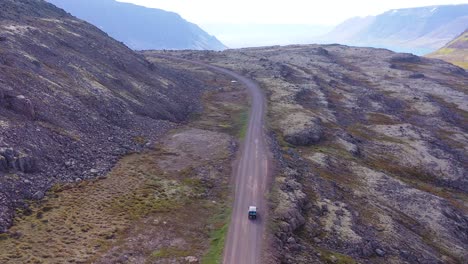 Aufsteigende-Antenne-über-Einem-Schwarzen-Wohnmobil,-Das-Auf-Einer-Unbefestigten-Straße-In-Island-In-Den-Nordwestfjorden-Unterwegs-Ist