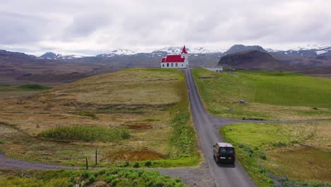 Aerial-over-a-black-camper-van-driving-up-to-a-church-on-a-hill-in-the-mountains-of-Iceland