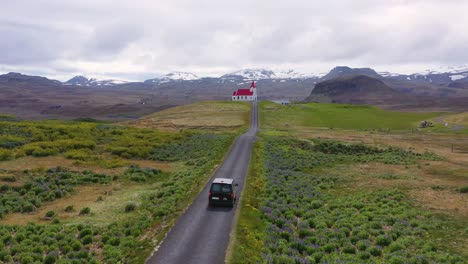 Aerial-over-a-black-camper-van-driving-up-to-a-church-on-a-hill-in-the-mountains-of-Iceland-1