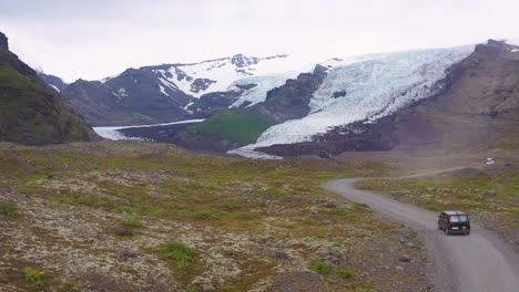Vista-Aérea-over-a-black-camper-van-conduciendo-up-to-a-remote-glacier-in-the-mountains-of-Iceland-1