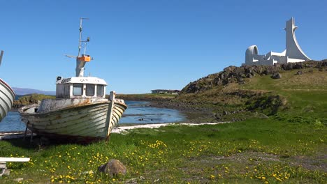 An-abandoned-landlocked-fishing-boat-with-modernist-architecture-of-Stykkish_____‚lmskirkja-church-Iceland