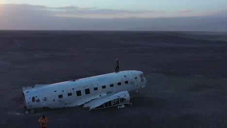 Aerial-man-standing-on-a-crashed-US-Navy-DC-3-on-the-black-sands-of-Solheimasandur-Iceland-1