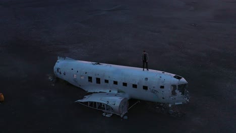 Aerial-man-standing-on-a-crashed-US-Navy-DC-3-on-the-black-sands-of-Solheimasandur-Iceland-2