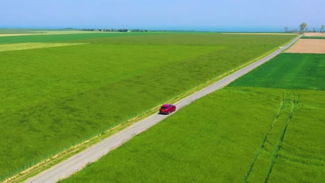 Aerial-of-a-red-car-traveling-through-green-fields-of-Normandy-France