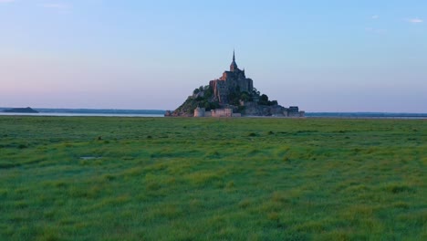 Beautiful-daytime-rising-aerial-over-fields-of-grass-with-Mont-Saint-Michel-monastery-in-Normandy-France-background