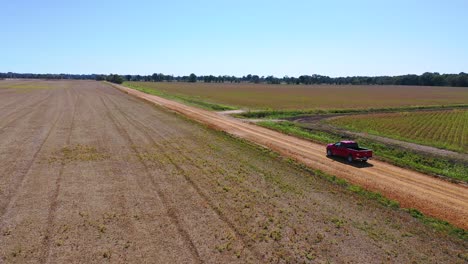 Aerial-shot-of-a-red-pickup-truck-traveling-on-a-dirt-road-in-a-rural-farm-area-of-Mississippi-1