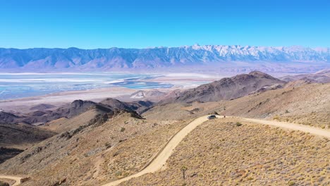 Aerial-of-a-4WD-wheel-drive-vehicle-on-a-dirt-road-through-the-Eastern-Sierras-with-Mt-Whitney-and-the-Owens-Valley-desert-and-dry-lake-bed-distant