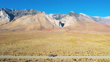 Aerial-of-a-4WD-wheel-drive-vehicle-on-a-road-in-front-of-the-Eastern-Sierras-with-Mt-Whitney-in-ther-distance-suggesting-remote-road-trip-adventure