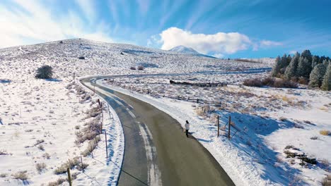 2020---aerial-of-a-cleared-woman-walking-dog-along-snow-covered-mountain-road-in-the-Eastern-Sierra-Nevada-mountains-near-Mammoth-lakes-California-1