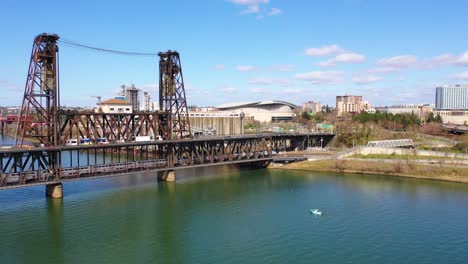 Schöne-Antenne-Des-Amtrak-Personenzuges,-Der-Die-Brücke-überquert-Und-In-Portland-Oregon-Mit-Stadtbahn-Oben-Und-Moda-Center-Hintergrund-Ankommt