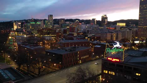 Night-aerial-past-Portland-Oregon-stag-deer-sign-and-downtown-old-town-cityscape-and-business-district