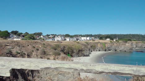 Beautiful-dolly-shot--wooden-fence-frames-a-blue-sky-day-view-of-a-small-beach-and-historic-buildings-Mendicino-CA-4