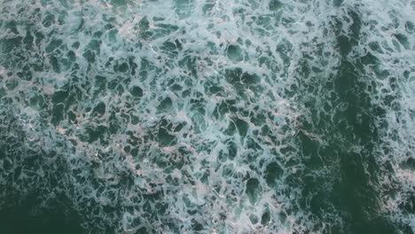 Aerial-perspective-looking-straight-down-at-the-ocean-with-waves-rolling-in