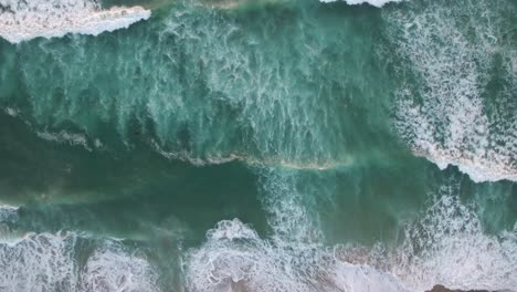 An-aerial-perspective-looking-straight-down-at-the-ocean-with-waves-rolling-in