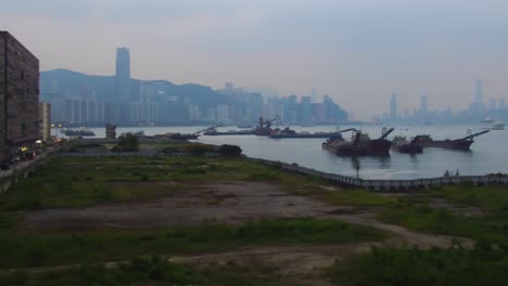 Schwenk-über-Den-Hafen-Von-Hongkong-Bei-Nebligen,-Dunstigen-Und-Smogigen-Bedingungen-Mit-Lastkähnen-Und-Booten-Im-Vordergrund