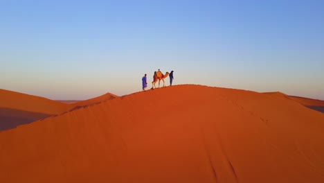 Eine-Bemerkenswerte-Antenne-über-Einem-Mann,-Der-Sein-Kamel-Bei-Sonnenaufgang-In-Marokko-über-Wüstensanddünen-Führt