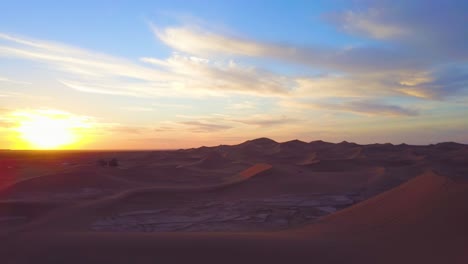 Eine-Bemerkenswerte-Luftaufnahme-über-Wüstensanddünen-Und-Ein-Kleines-Dorf-Bei-Sonnenaufgang-In-Marokko-1