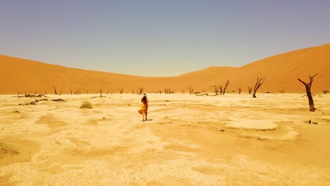 Antena-Siguiendo-A-Una-Mujer-Corriendo-Cerca-De-árboles-Muertos-En-Sossusvlei-Desierto-Dunas-De-Arena-En-El-Desierto-De-Namib,-Namibia,-África