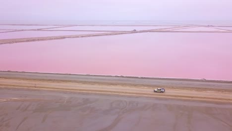 Aerial-over-a-4WD-safari-vehicle-driving-on-a-colorful-pink-salt-flat-region-in-Namibia-Africa