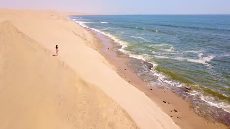 Antena-Sobre-Un-Modelo-Liberado-Mujer-Caminando-Sobre-Magníficas-Dunas-De-Arena-En-La-Costa-De-Los-Esqueletos-Namibia-1