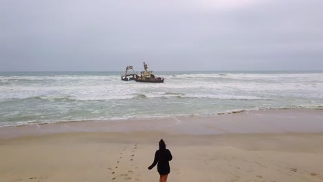 Amazing-aerial-over-a-woman-jogging-or-running-towards-a-shipwreck-along-the-Skeleton-Coast-of-Namibia-Africa-1