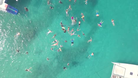 Rising-aerial-of-large-group-of-tourists-snorkling-and-diving-on-the-Caribbean-island-of-Barbados-off-a-large-catamaran-boat