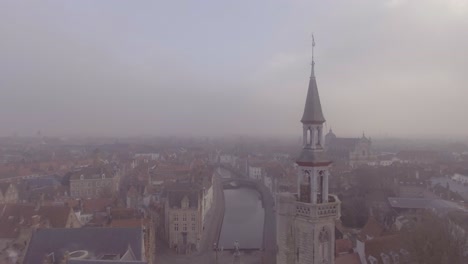 Aerial-of-a-mysterious-foggy-day-in-Bruges-Belgium-with-cathedral-churches-and-spires-in-distance
