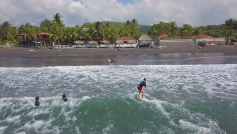 Aerial-drone-shot-over-surfers-enjoying-the-surf-on-the-coast-of-El-Salvador