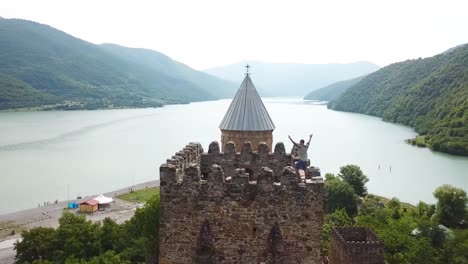 Antena-Alrededor-De-Un-Hombre-De-Pie-Sobre-Un-Hermoso-Castillo-En-El-Lago-Zhinvali-En-La-República-De-Georgia